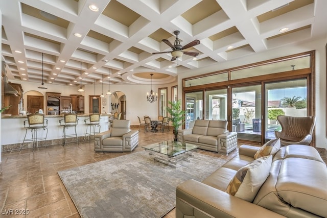 living room featuring ceiling fan with notable chandelier, arched walkways, beamed ceiling, and coffered ceiling