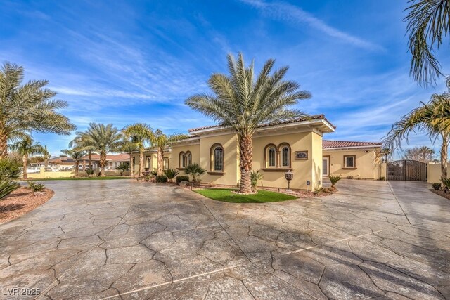 mediterranean / spanish-style house with curved driveway, a gate, stucco siding, and a tiled roof