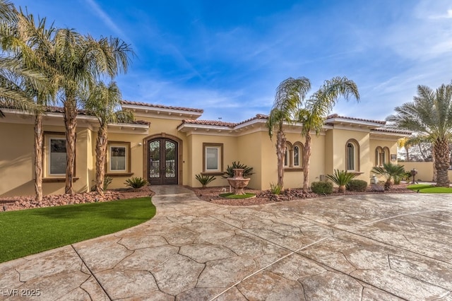 mediterranean / spanish-style home featuring french doors, stucco siding, a front lawn, and a tiled roof