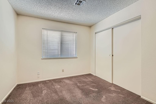 unfurnished bedroom featuring a textured ceiling, visible vents, baseboards, a closet, and carpet flooring