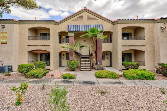 view of front of home featuring stairway, central AC unit, a tile roof, and stucco siding