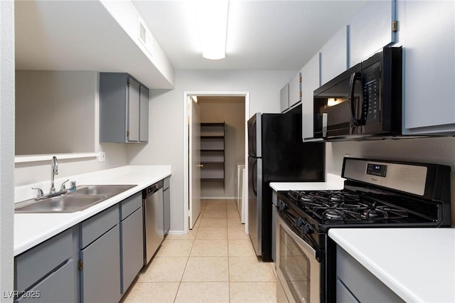 kitchen with light tile patterned flooring, light countertops, a sink, appliances with stainless steel finishes, and gray cabinetry