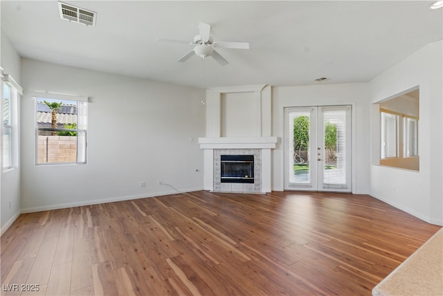 unfurnished living room with ceiling fan, visible vents, a tile fireplace, wood finished floors, and baseboards