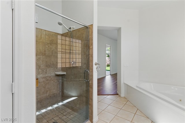 bathroom featuring tile patterned flooring, a bath, baseboards, and a stall shower