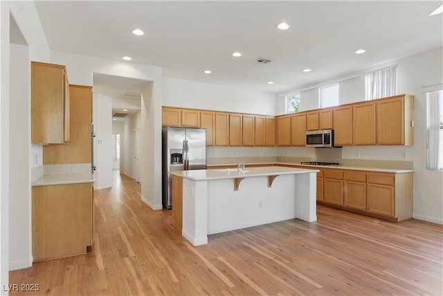 kitchen with a kitchen bar, visible vents, appliances with stainless steel finishes, light countertops, and an island with sink