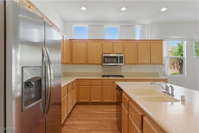 kitchen with appliances with stainless steel finishes, a sink, light wood finished floors, and light brown cabinets