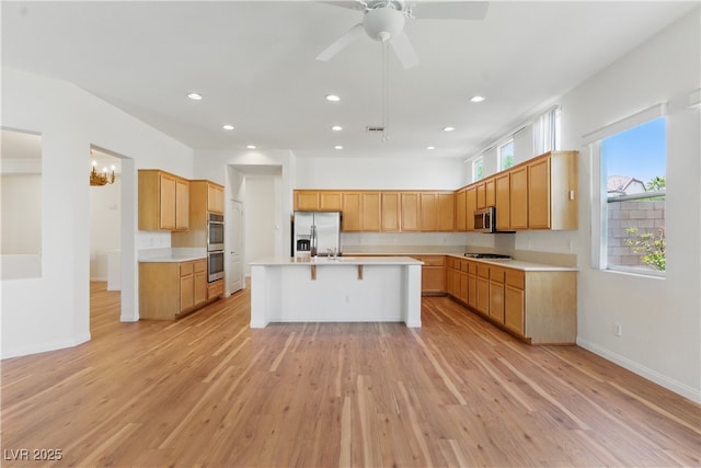kitchen with light countertops, stainless steel appliances, light wood finished floors, and a kitchen bar