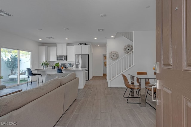 living room featuring stairs, recessed lighting, visible vents, and light wood-type flooring