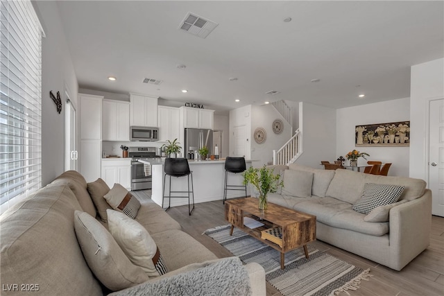 living area with recessed lighting, visible vents, stairway, and light wood-type flooring