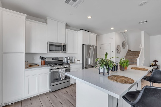kitchen featuring appliances with stainless steel finishes, a center island with sink, a kitchen bar, and visible vents