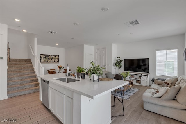 kitchen featuring open floor plan, white cabinetry, a sink, light wood finished floors, and dishwasher
