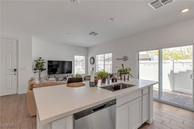 kitchen featuring stainless steel dishwasher, a sink, white cabinets, and visible vents