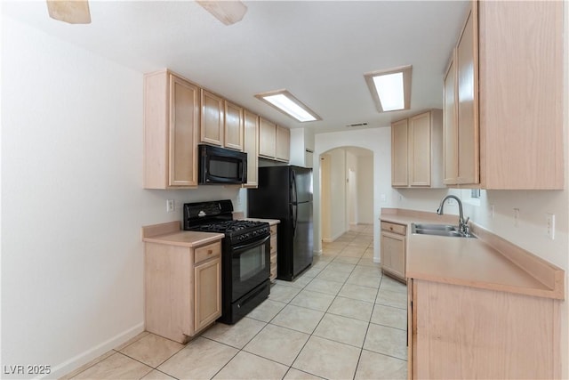 kitchen with arched walkways, a sink, black appliances, light brown cabinets, and light tile patterned flooring