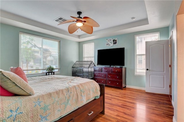 bedroom with baseboards, a tray ceiling, light wood-type flooring, and visible vents