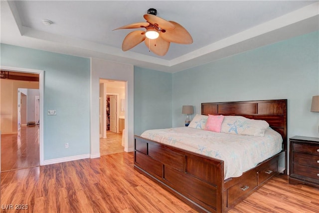 bedroom with light wood-style floors, baseboards, and a tray ceiling