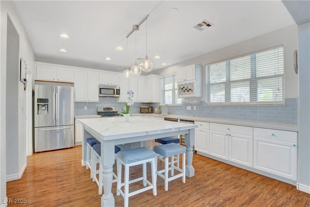 kitchen with white cabinets, stainless steel appliances, tasteful backsplash, and visible vents