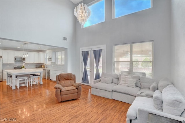 living room with a high ceiling, a chandelier, visible vents, and light wood-style floors