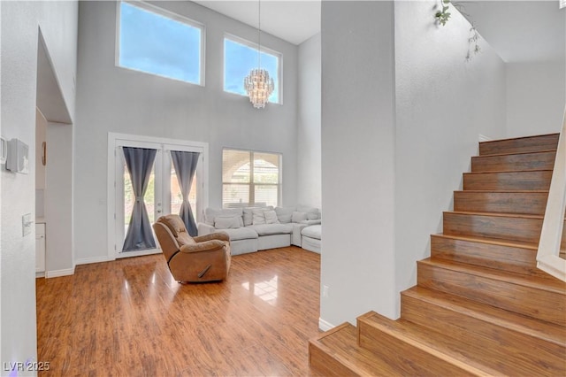stairs with an inviting chandelier, baseboards, a high ceiling, and wood finished floors