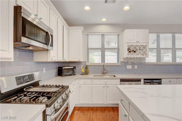 kitchen with light wood-type flooring, white cabinetry, tasteful backsplash, a sink, and appliances with stainless steel finishes