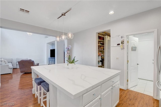 kitchen featuring visible vents, light wood-style flooring, white cabinetry, and light stone countertops
