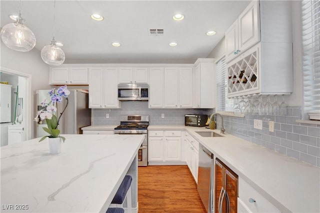 kitchen featuring backsplash, visible vents, appliances with stainless steel finishes, a sink, and beverage cooler