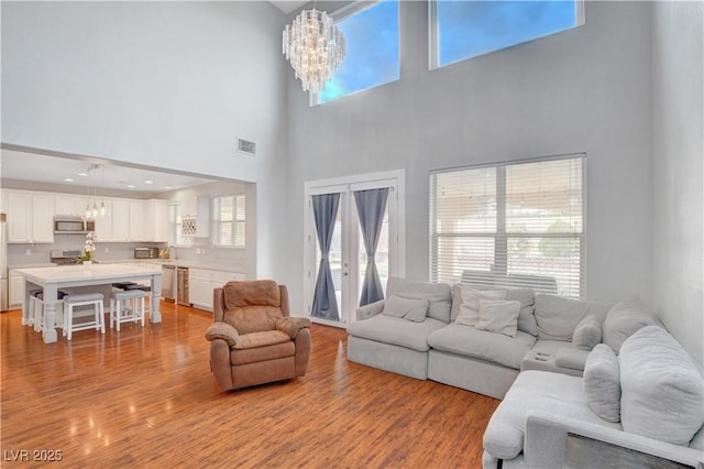 living room with an inviting chandelier, light wood-style floors, a towering ceiling, and visible vents