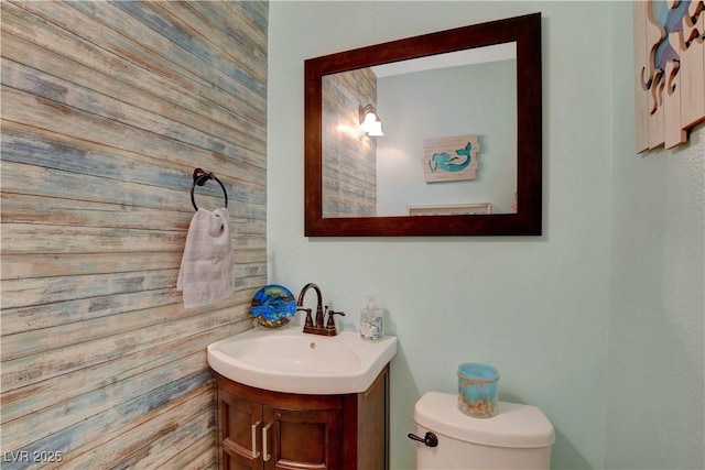 half bathroom with vanity, wooden walls, and toilet
