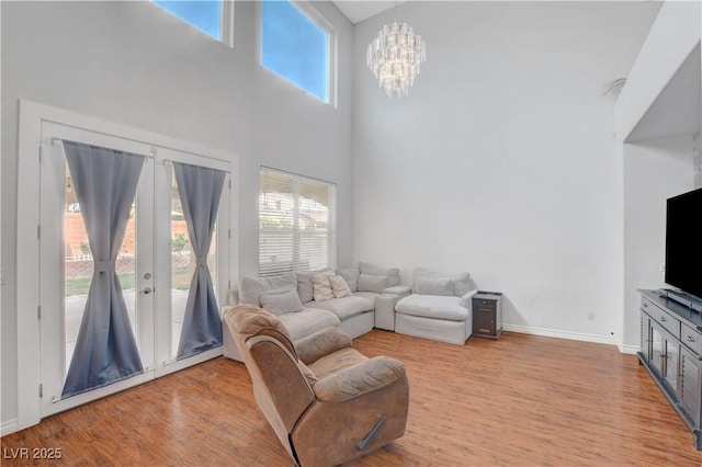 living room featuring a high ceiling, an inviting chandelier, baseboards, and light wood finished floors