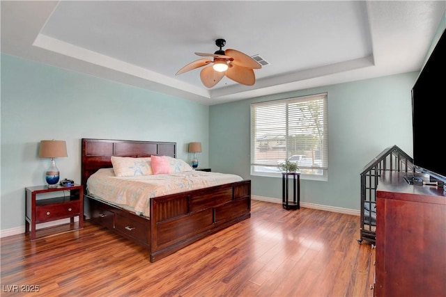 bedroom with a raised ceiling, baseboards, wood finished floors, and visible vents