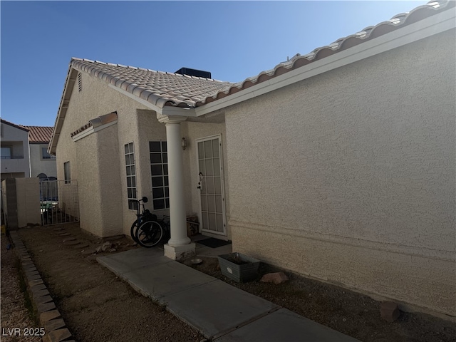 view of exterior entry featuring fence, a tiled roof, and stucco siding
