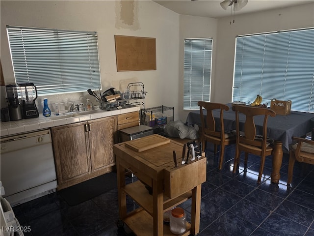 kitchen with dark tile patterned floors, a ceiling fan, tile countertops, dishwasher, and a sink