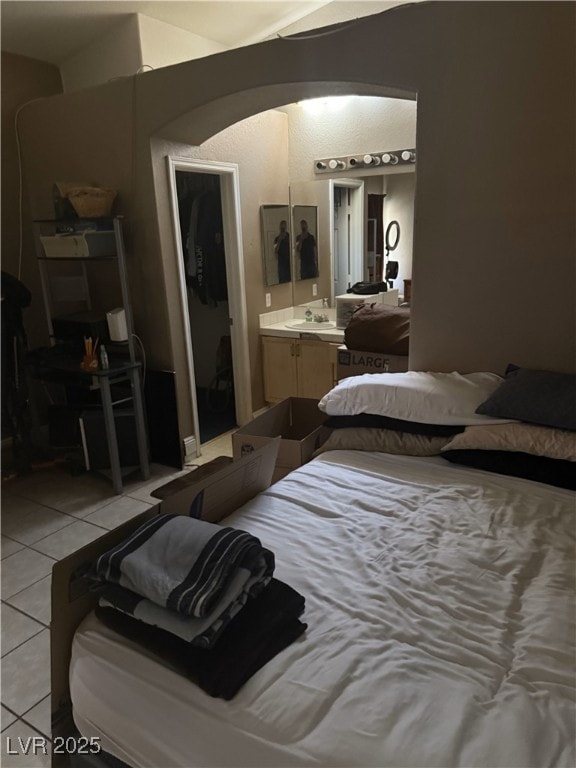 bedroom featuring light tile patterned floors, arched walkways, a sink, and connected bathroom