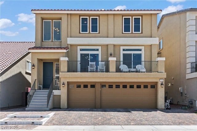 view of property with decorative driveway, a garage, stucco siding, and a tiled roof