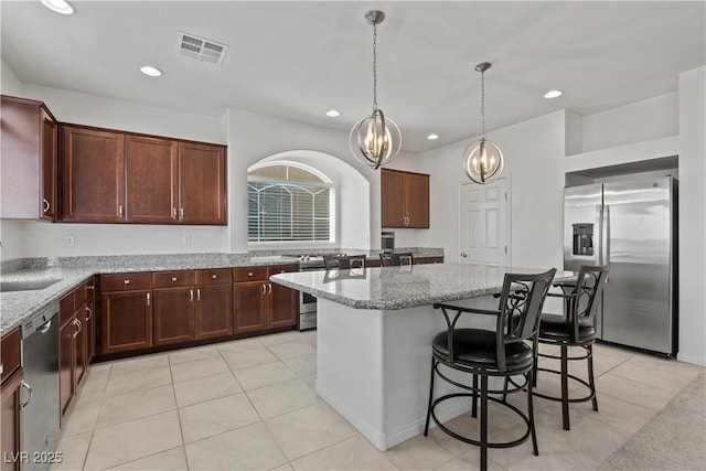 kitchen featuring visible vents, an inviting chandelier, a center island, light stone counters, and stainless steel appliances