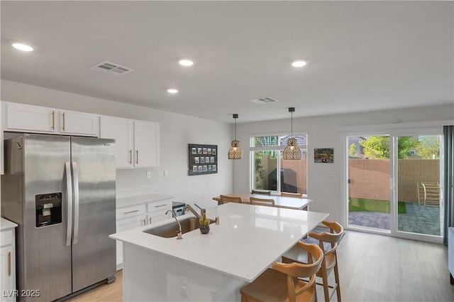 kitchen featuring light wood-style floors, visible vents, a sink, stainless steel fridge, and white cabinetry
