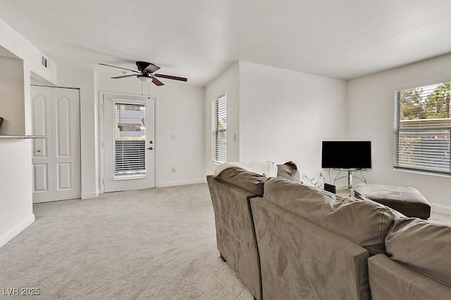 living area featuring baseboards, ceiling fan, light carpet, and a wealth of natural light