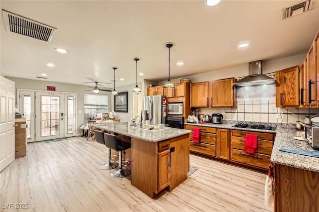 517 7th St, Boulder City, NV 89005 - kitchen featuring black appliances, wall chimney range hood, brown cabinets, a center island, and light wood-style floors