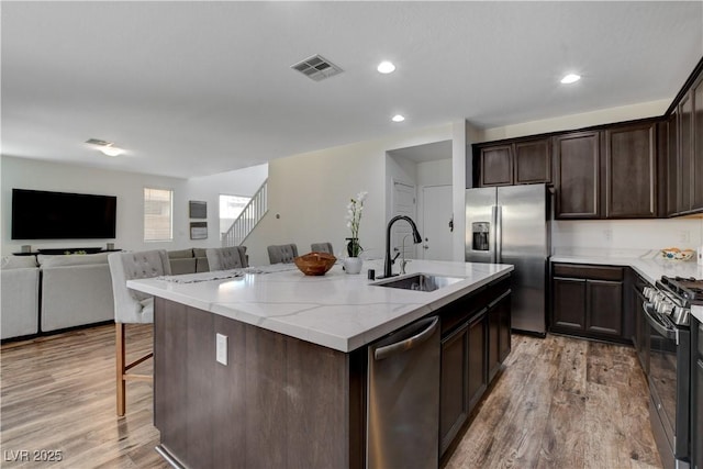 kitchen featuring visible vents, appliances with stainless steel finishes, light stone countertops, a sink, and light wood-style flooring