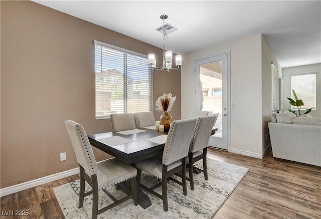 dining space with baseboards, visible vents, wood finished floors, and a notable chandelier