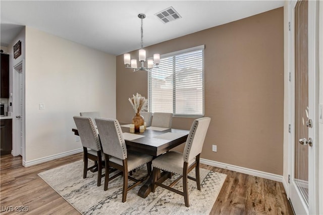 dining space with baseboards, light wood finished floors, a chandelier, and visible vents