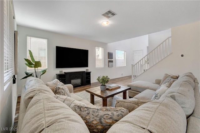 living area featuring a healthy amount of sunlight, stairs, wood finished floors, and visible vents