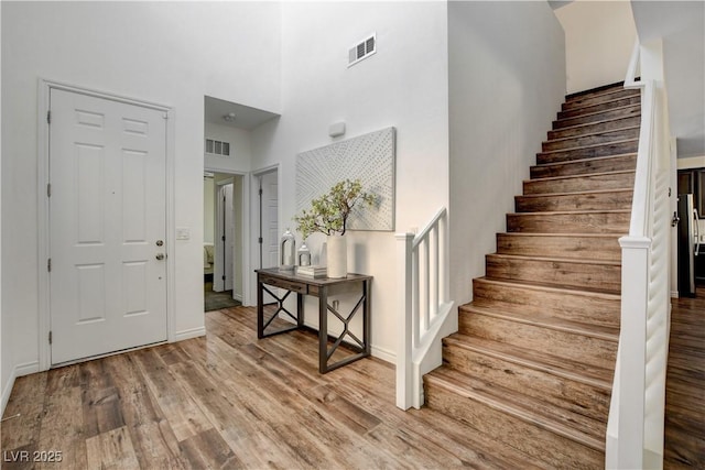 foyer featuring visible vents, a towering ceiling, wood finished floors, and stairway