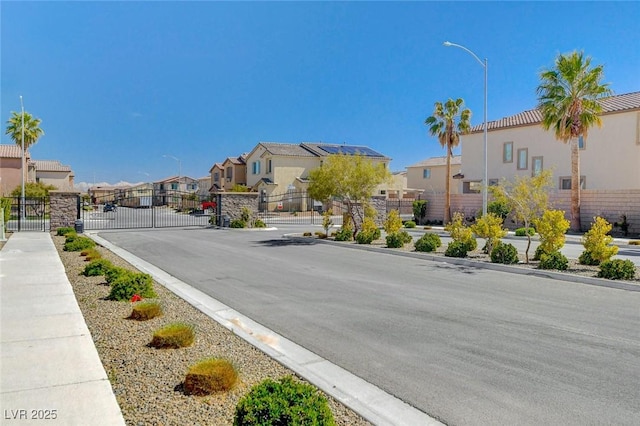 view of road with a residential view, street lighting, sidewalks, curbs, and a gate