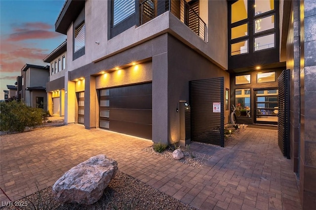 5436 Succulent Rose Dr, Las Vegas, NV 89135 - property exterior at dusk featuring an attached garage, decorative driveway, and stucco siding