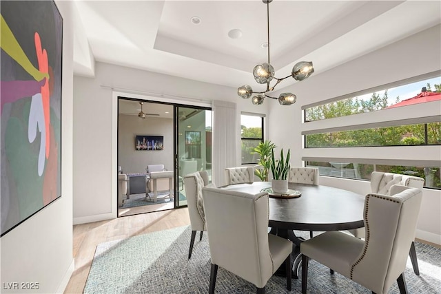 dining area featuring baseboards, a notable chandelier, a raised ceiling, and light wood-style floors