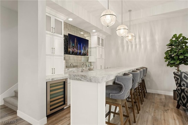 bar with stairs, beverage cooler, baseboards, light wood-type flooring, and wet bar