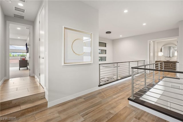 hall featuring visible vents, wood finished floors, baseboards, an upstairs landing, and recessed lighting
