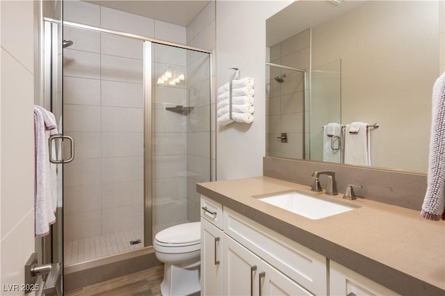 bathroom with vanity, wood finished floors, toilet, and a shower stall