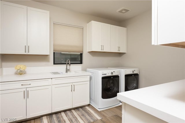washroom featuring cabinet space, a sink, light wood finished floors, visible vents, and washer and clothes dryer