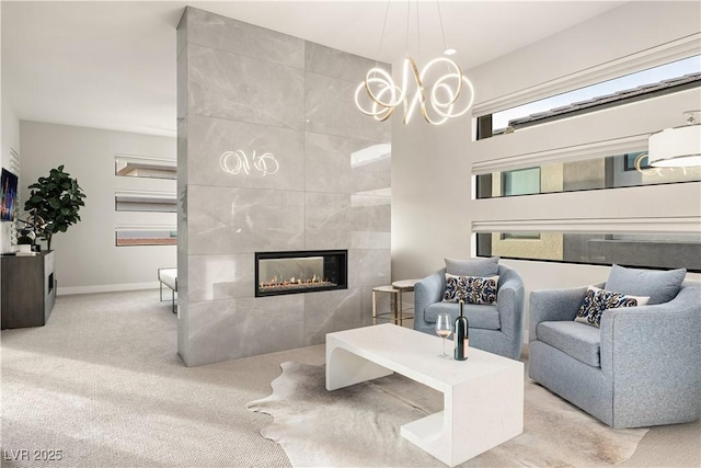 living area with a tiled fireplace, baseboards, an inviting chandelier, and carpet flooring